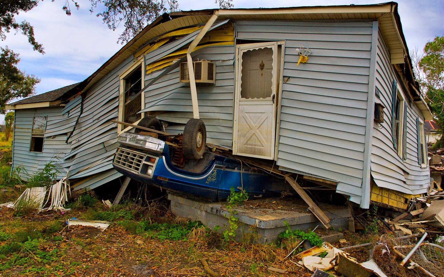 Single story house with blue siding that is severely damaged from a storm