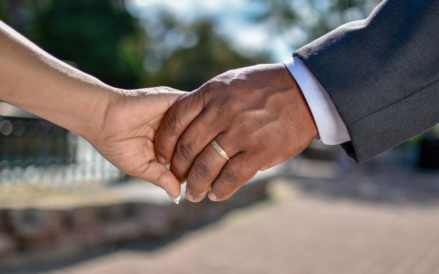 a close up photo of a couple holding hands featuring the man's wedding band